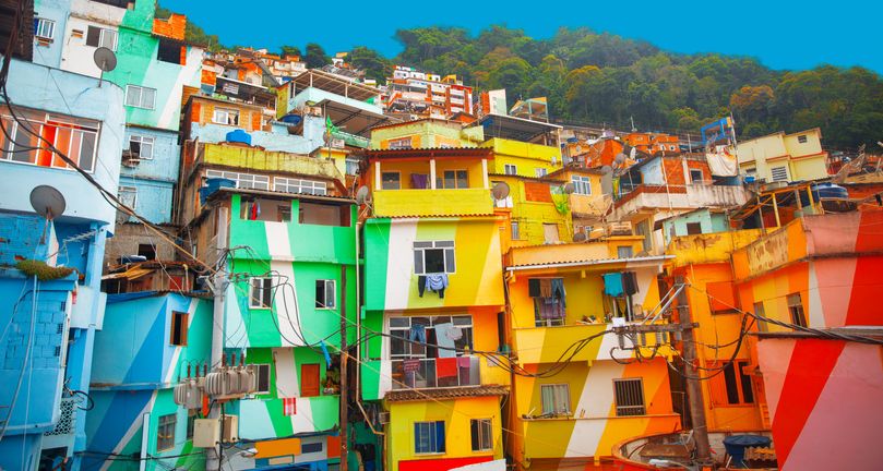 Bright green, yellow, orange and red buildings huddle together on a hillside in a favela in Rio de Janeiro, Brazil
