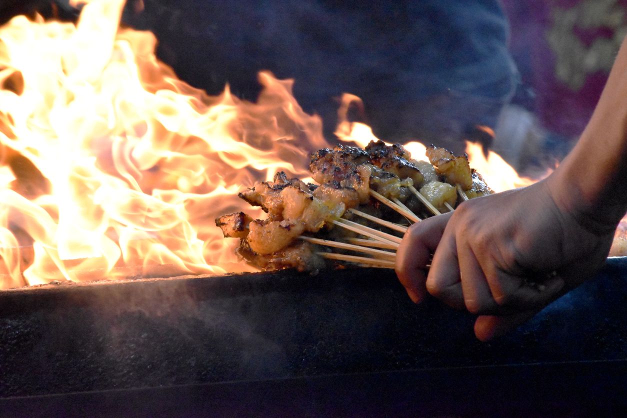 Close up of satay sticks held over flames in a cast iron BBQ 