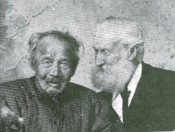 Black and white low quality photo of two old men – one Chinese, one European – smiling together