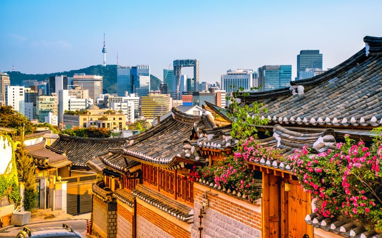 In the foreground, Bukchon Hanok Village with modern buildings in the background