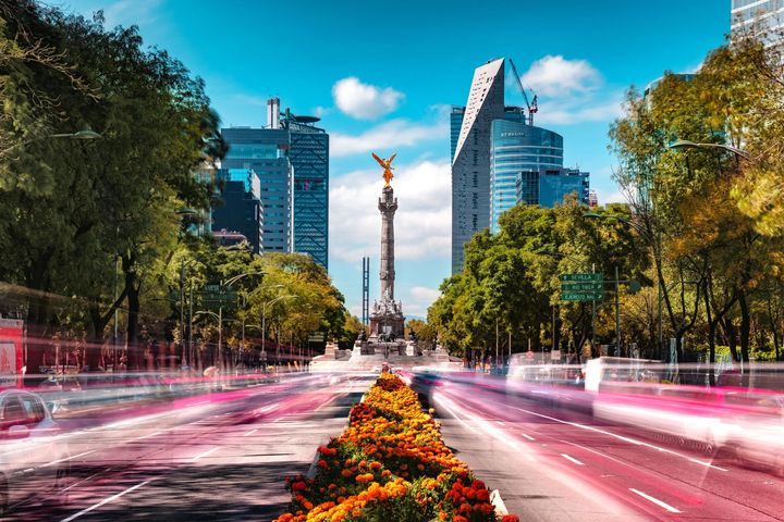 In Mexico City, from the median strip of the Paseo de la Reforma, red and orange flowers lead up to a tall plinth topeed b 