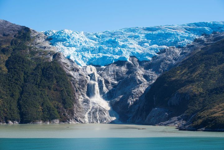 A glacier hugs a ridge and releases a waterfall into a fjord in Southern Chile 