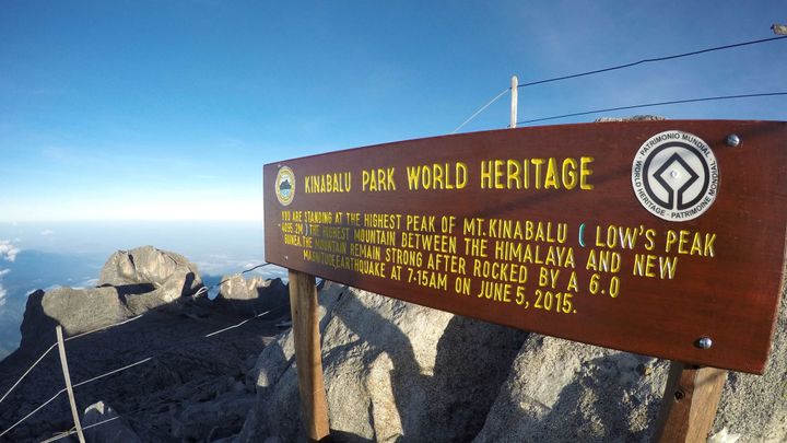 A wooden sign marks the rocky summit of Mount Kinabalu, with jungle in the far lower distance