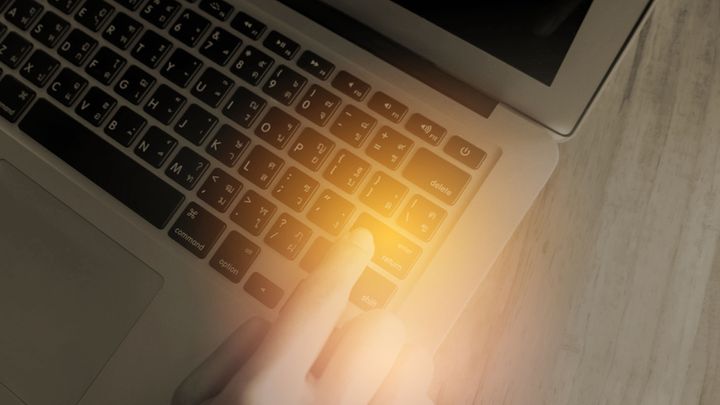 Close up of laptop keyboard, golden light shines on a finger pressing the enter button 