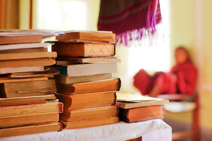 A stack of old books on a cloth covered table with background (out of focus) monk in red clothing, reading 